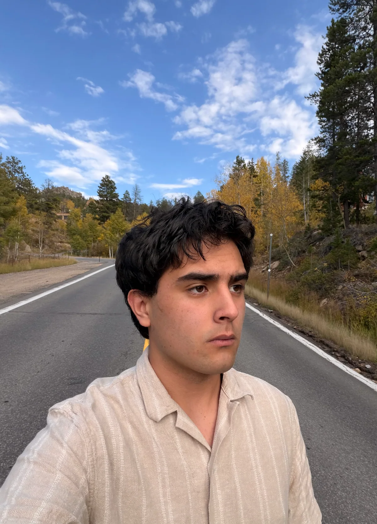 Benjamin Suitts on a road bordered by autumn trees beneath a blue sky.